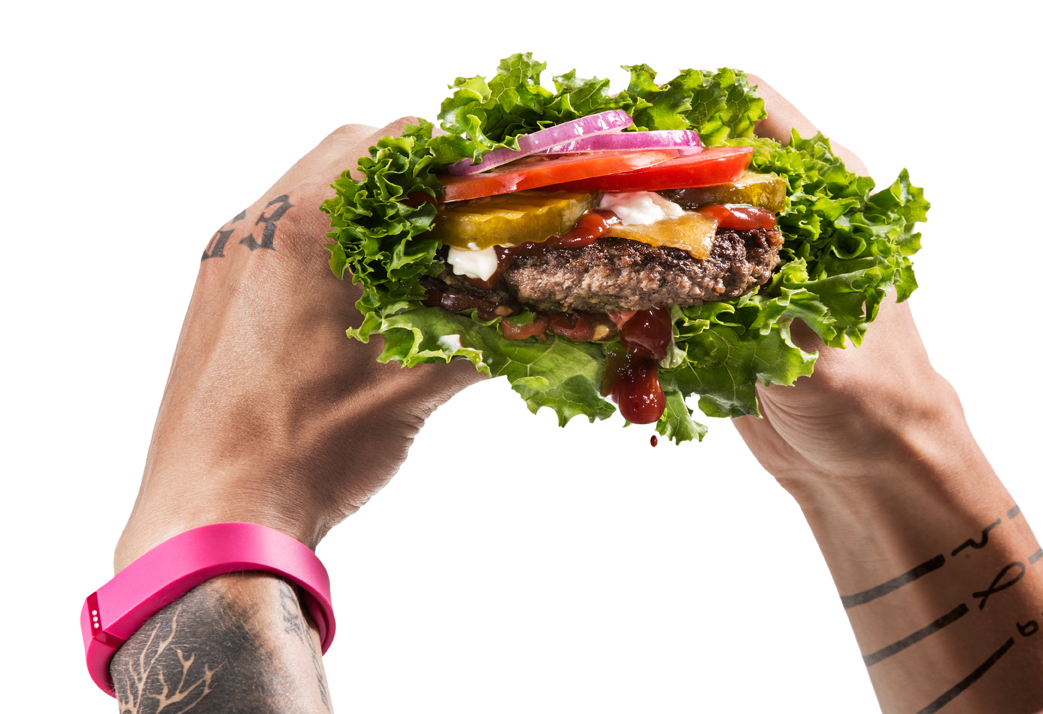 Photo of a man wearing a pink FitBit holding a dripping lettuce hamburger  — Studio 3, Inc.
