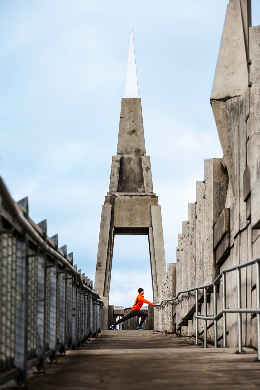 Runner in orange coat stretching in urban city landscape, tower behind  — Studio 3, Inc.