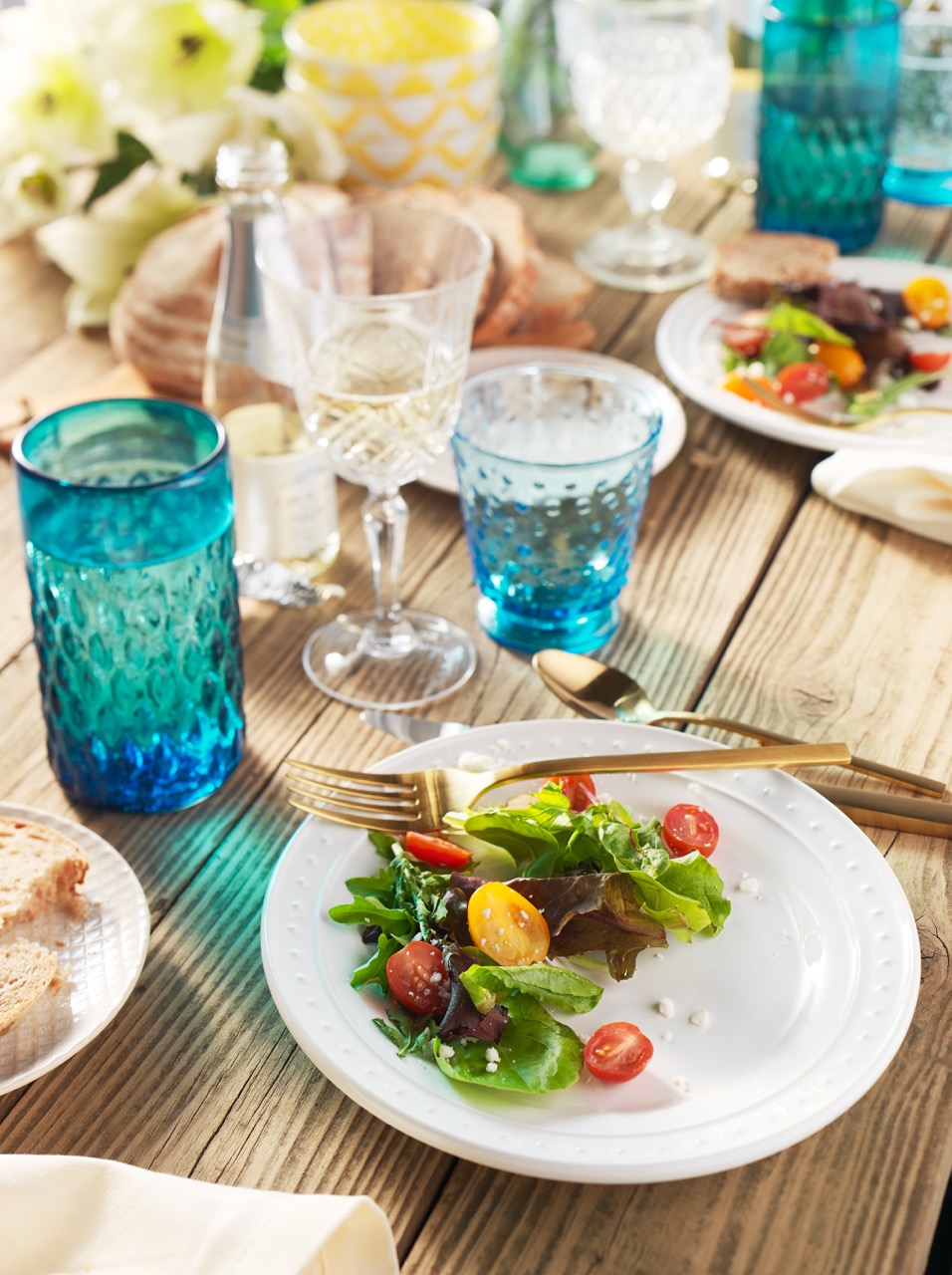 A garden party tabletop set with half eaten colorful Summer tomato salad food dish and colored glasses  — Studio 3, Inc.