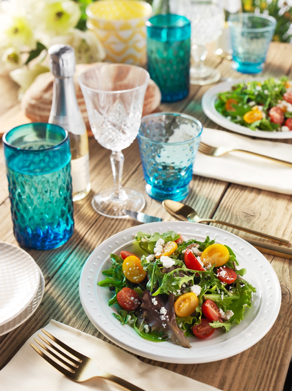 A garden party tabletop set with colorful Summer tomato salad dish and colored glasses  — Studio 3, Inc.