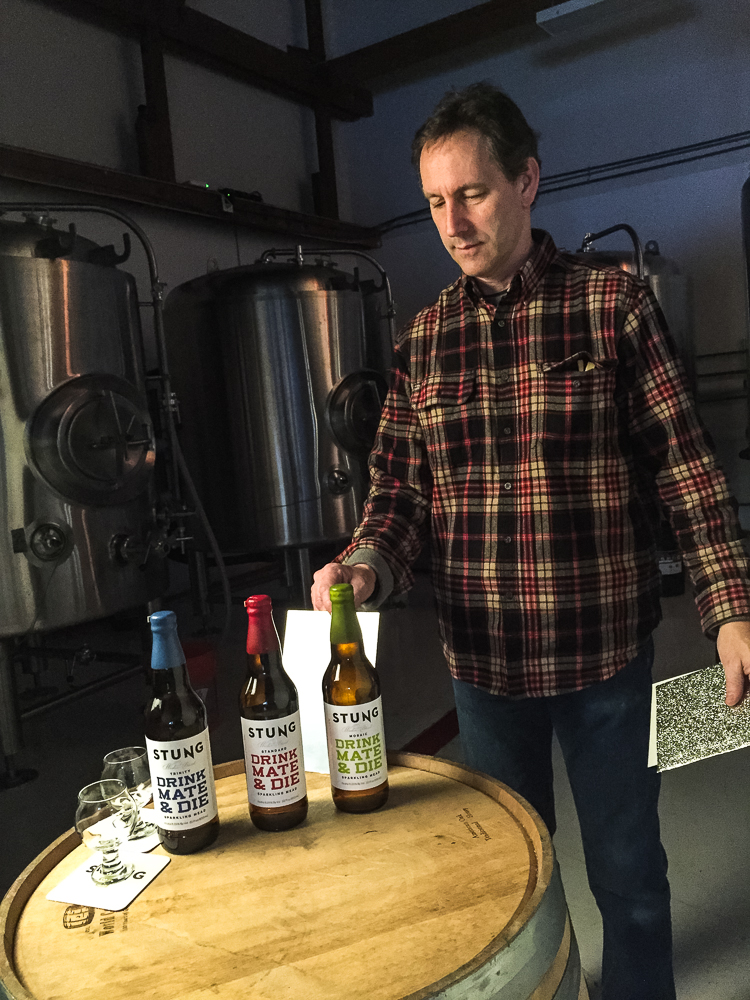 Photographer Craig Wagner positioning Stung Fermented mead bottle on barrel for product photography shoot on location  — Studio 3, Inc.