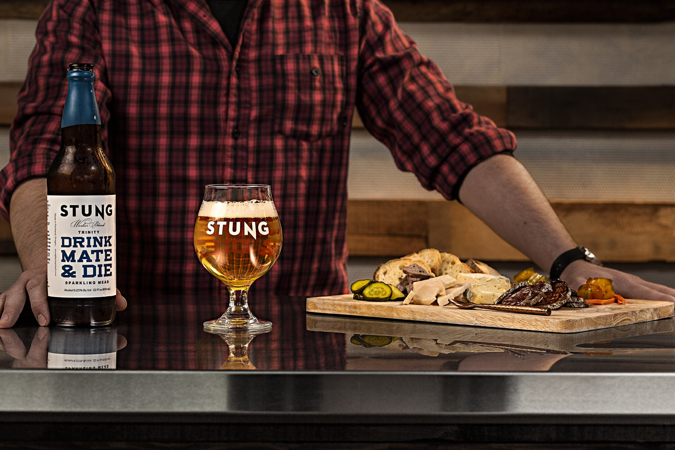 Stung Fermented Drink Mate & Die Mead in glass on table with meat and cheese party appetizer board  — Studio 3, Inc.