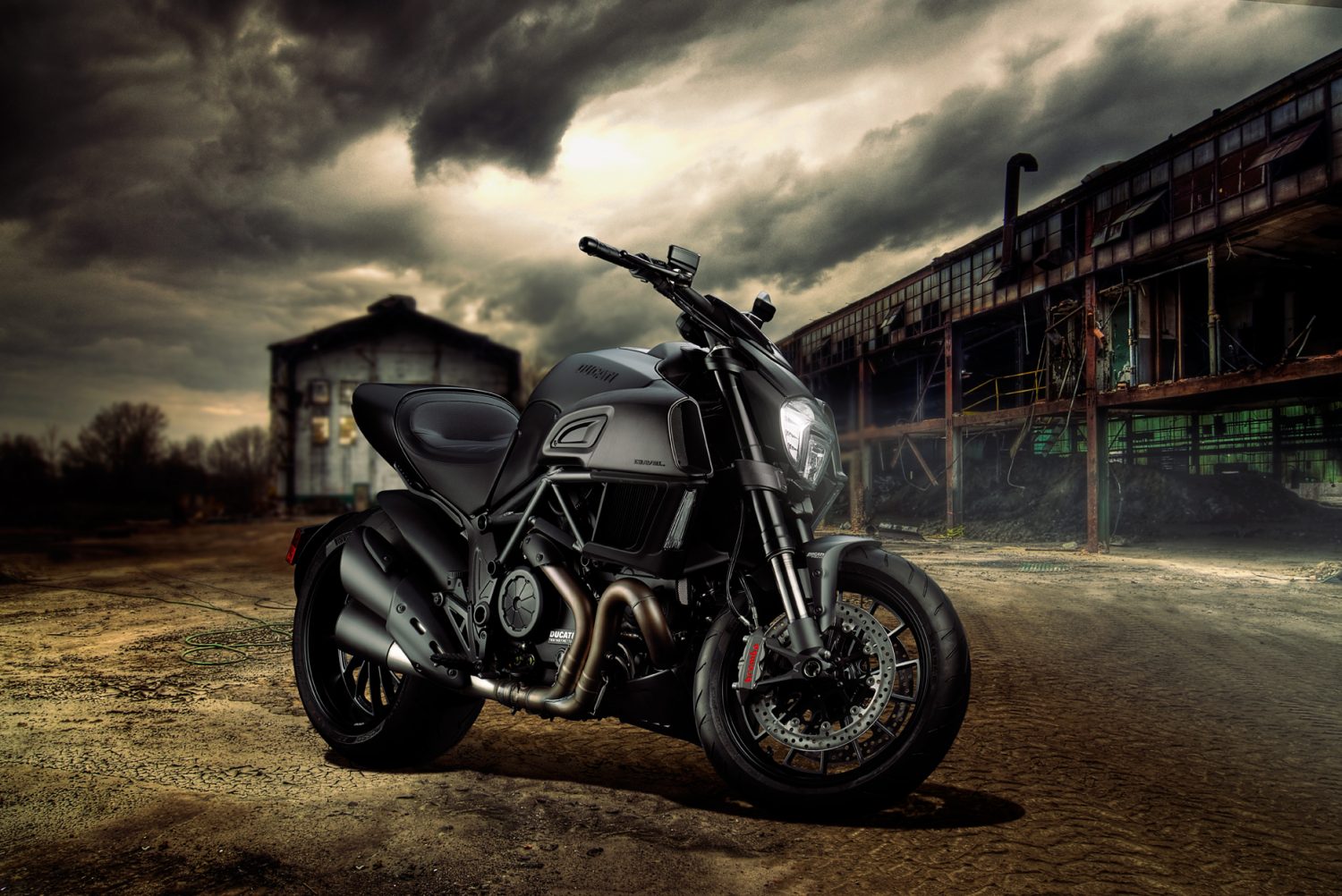 Black Ducati motorcycle in industrial location with dark stormy night sky behind