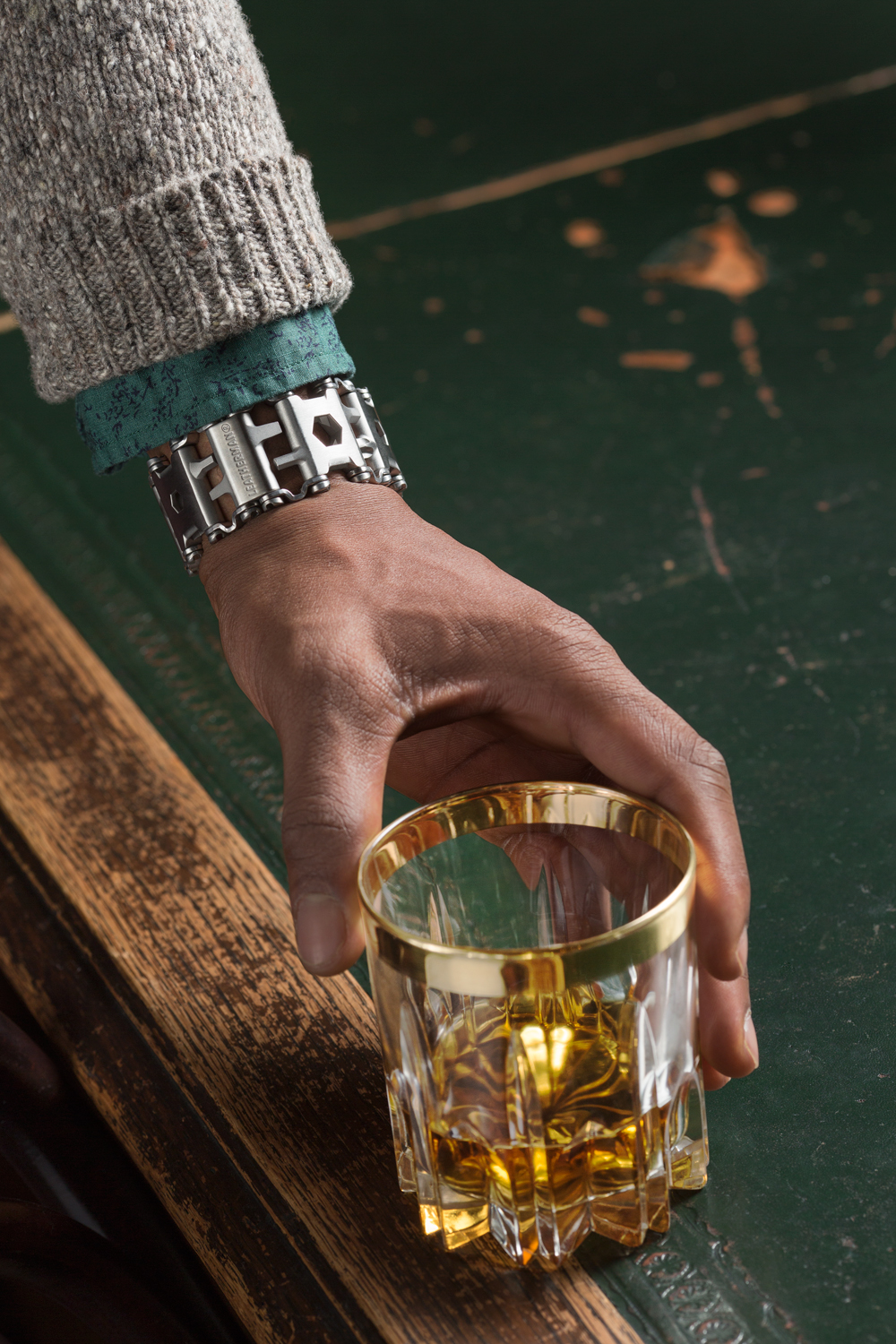 Arm wearing Leatherman tread tool bracelet reaching for cocktail drink on table