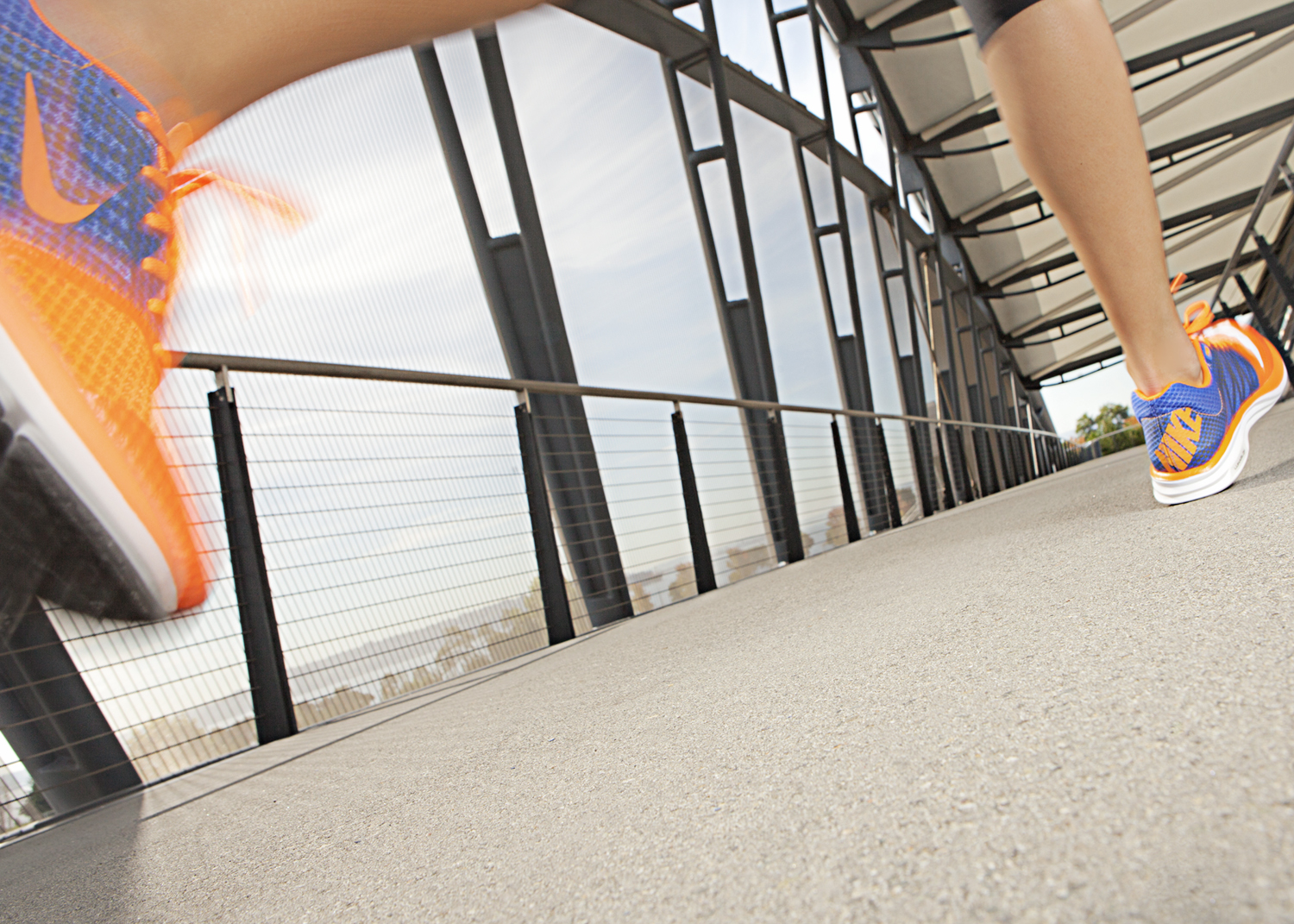 Close up of runner's feet wearing orange and blue Nike running sneakers, running down urban walkway