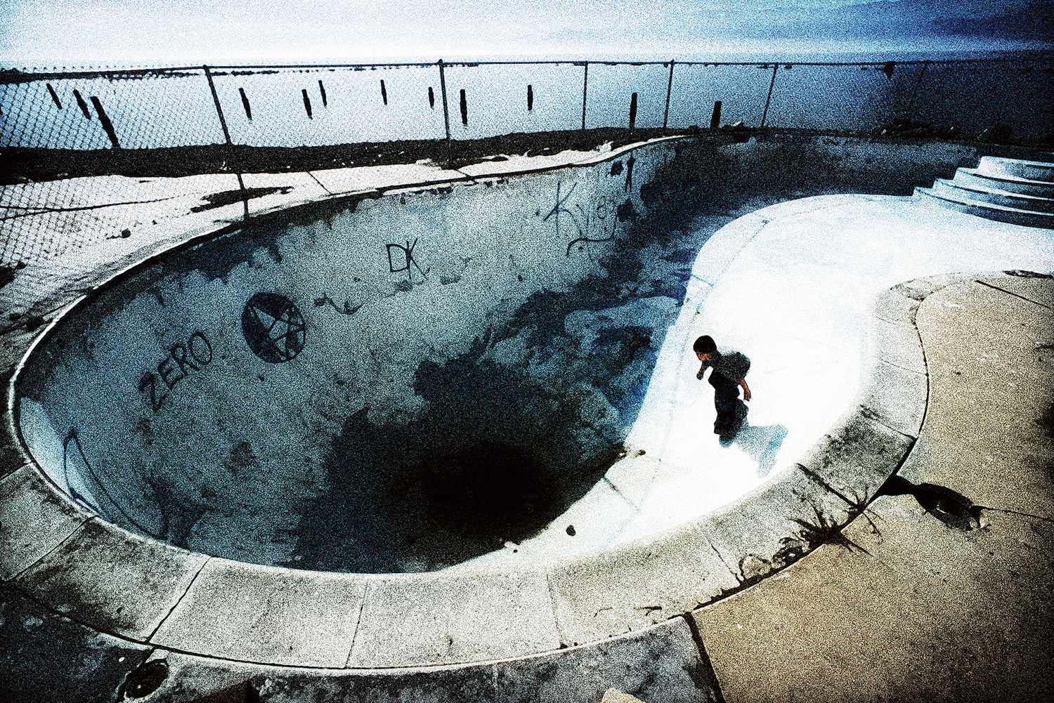 Gritty lifestyle photo of boy skateboarding on side of empty urban pool