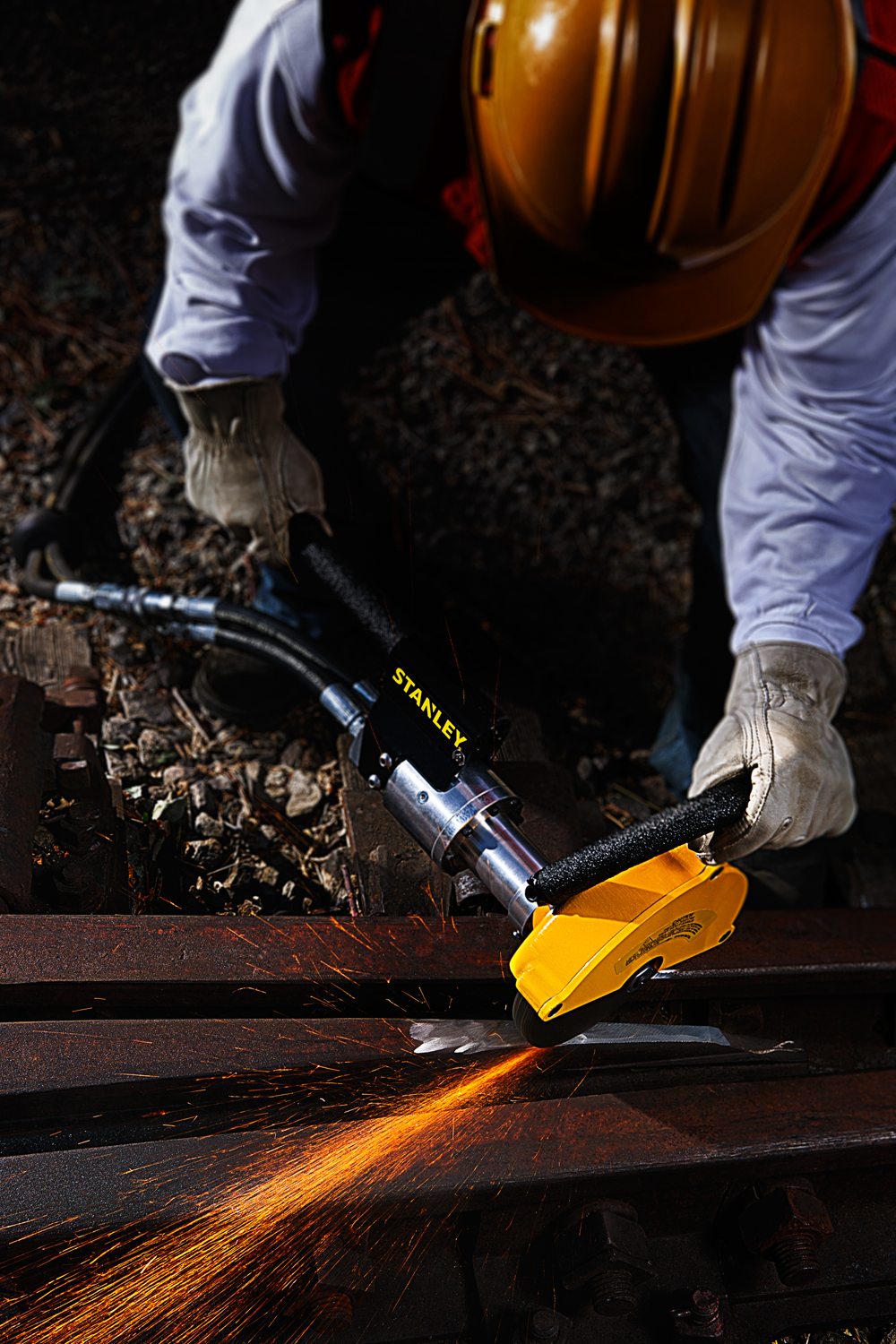 Construction worker polishing rust off railroad tie with Stanley pneumatic grinder tool, making sparks